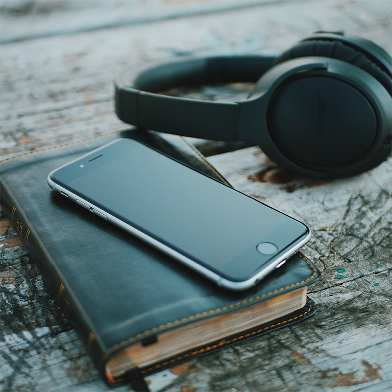 A bBible with a smart phone on top and a pair of headphones sitting near by.